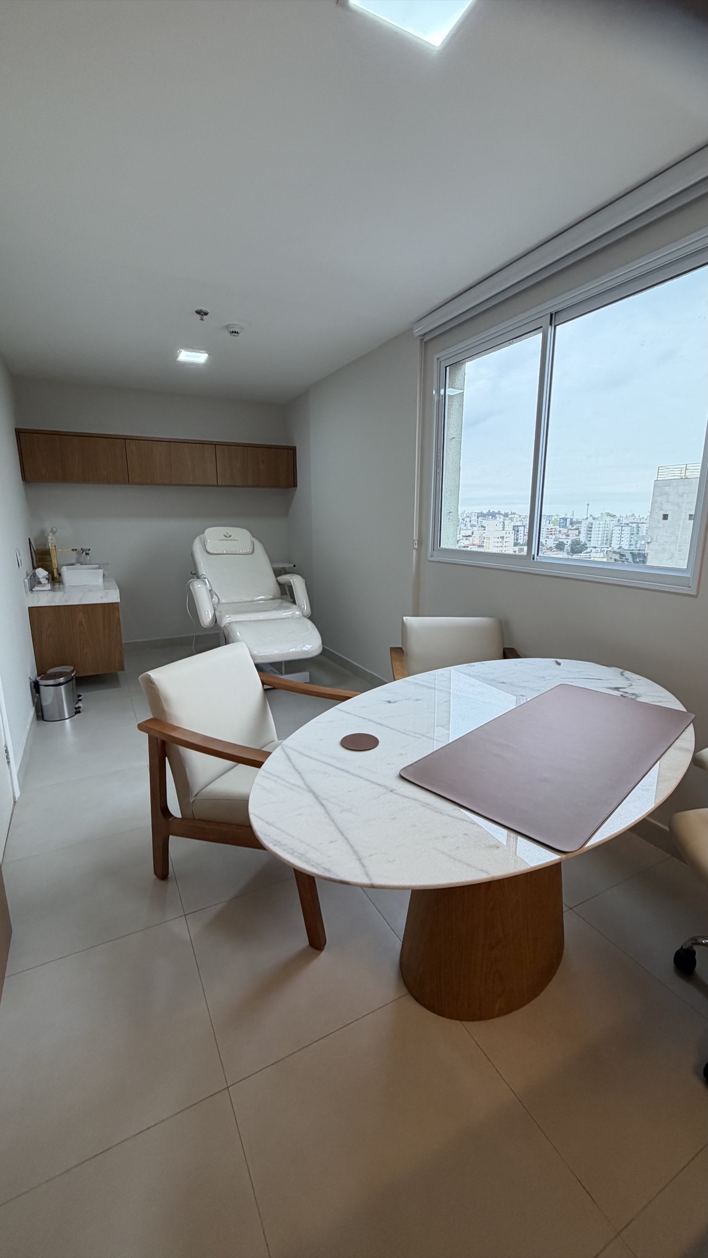 Consultório 02 com mesa redonda de mármore, poltronas e janela com vista